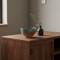 Bol en grès HINOKO bleu et sablé sur un meuble en bois, à côté d’un vase noir
