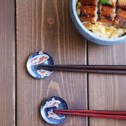 Deux repose-baguettes KOÏ sur une table en bois, avec baguettes et un bol d’unagi don